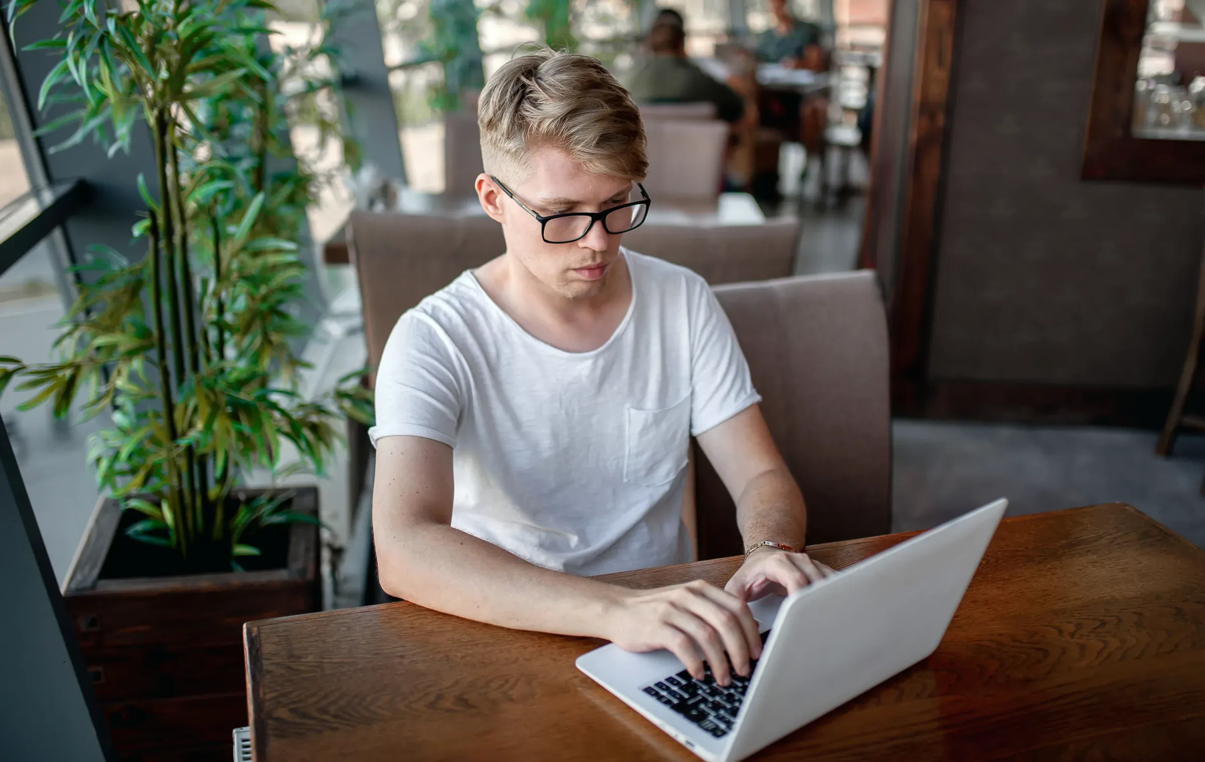Junger Mann arbeitet konzentriert am Laptop an einem Holztisch