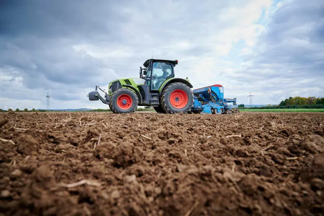 Traktor mit Sämaschine auf dem vorbereiteten Acker, im Vordergrund die groben Erdschollen