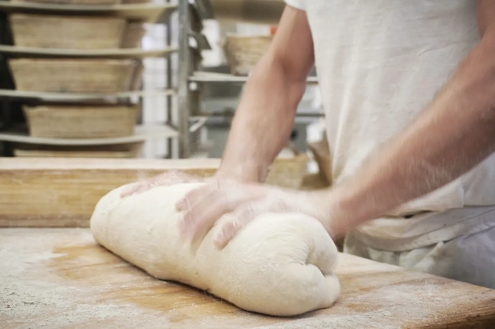 Hände wirken einen Ciabatta-Teigling auf dem bemehlten Holzbrett lang