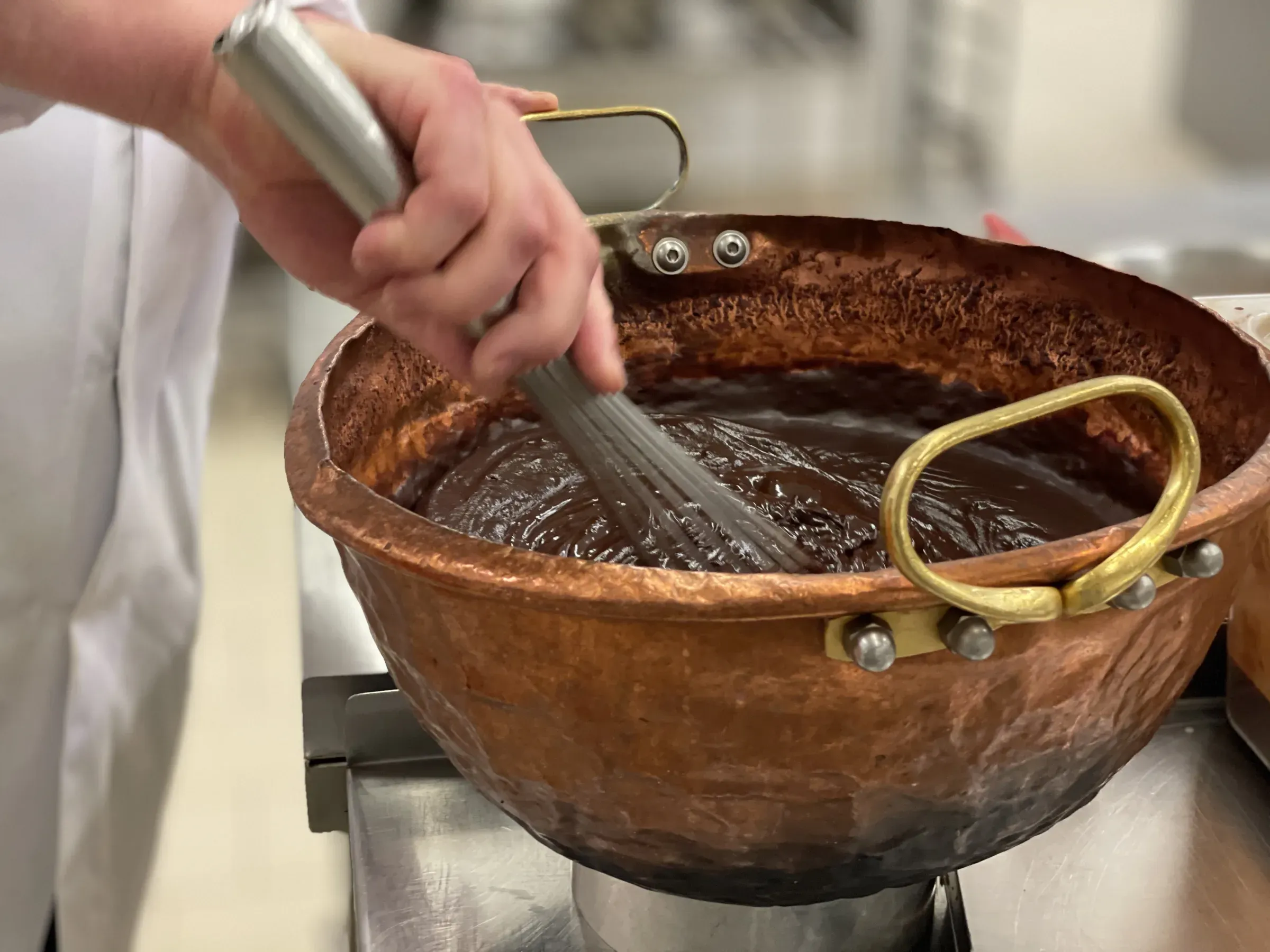 Hand rührt mit dem Schneebesen Kuvertüre im kupfernen Kessel