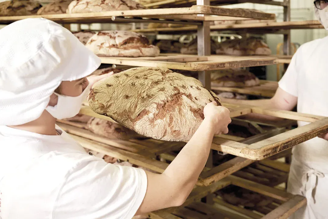 Auszubildende legt ein großes Brot auf einen Holzwagen in der Backstube