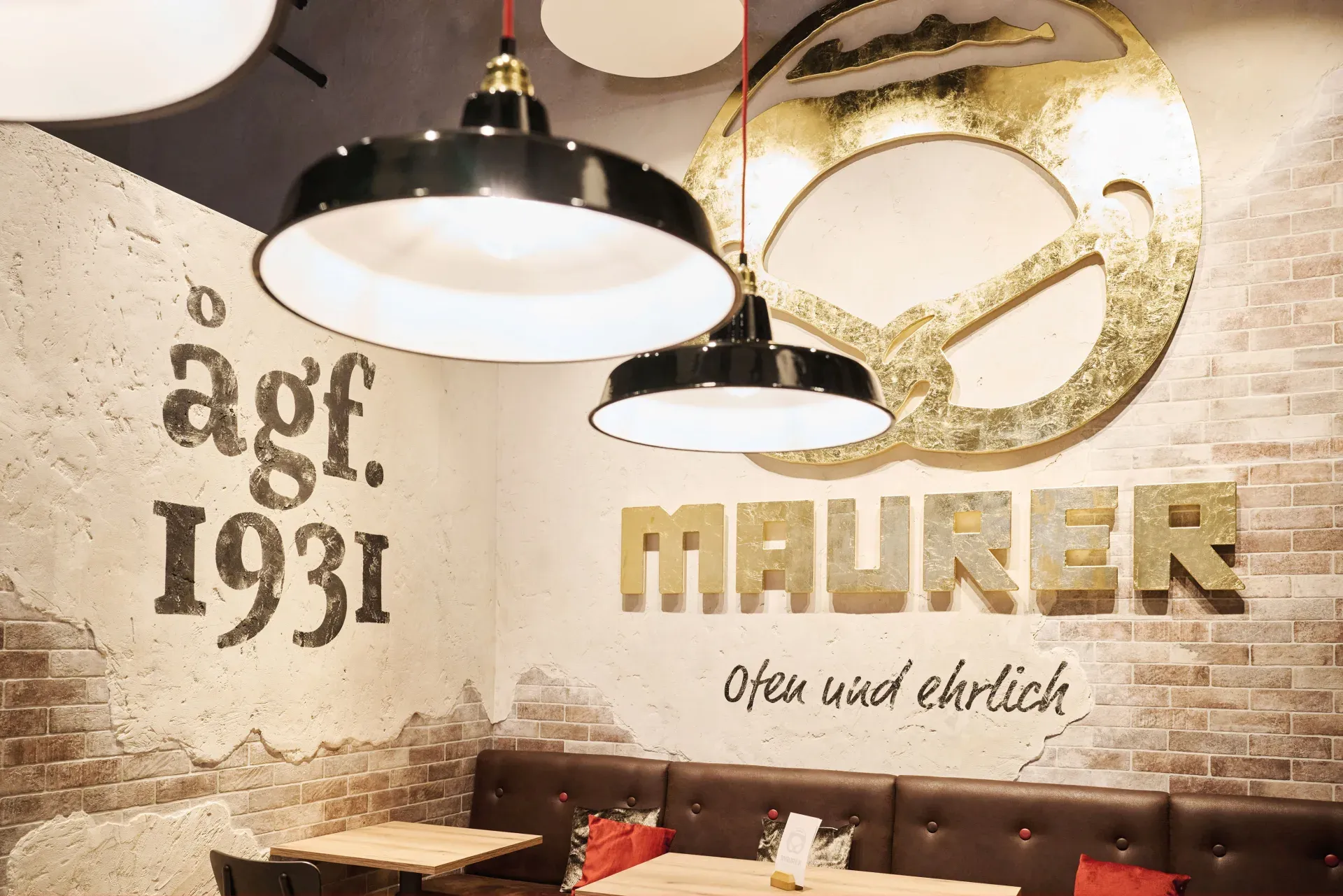 Wand im Bäckerei-Café Schorndorf mit dem goldenen Maurer-Schriftzug, der Brezel und dem Gründungsjahr ågf 1931 darüber der Sitzbank