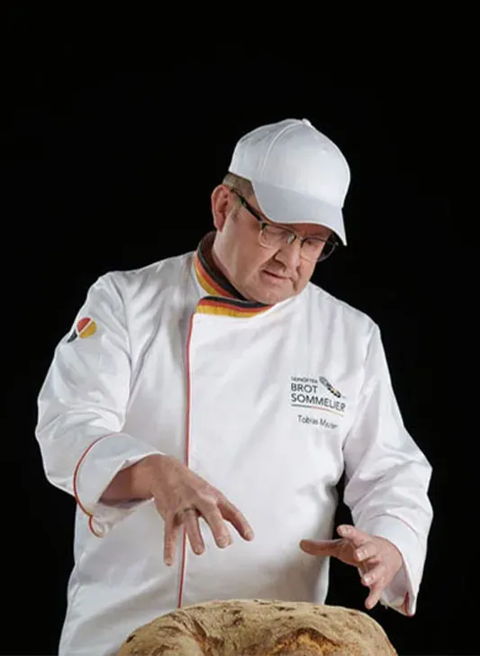 Tobias Maurer in der Sommelier-Jacke, in den Händen ein Brot