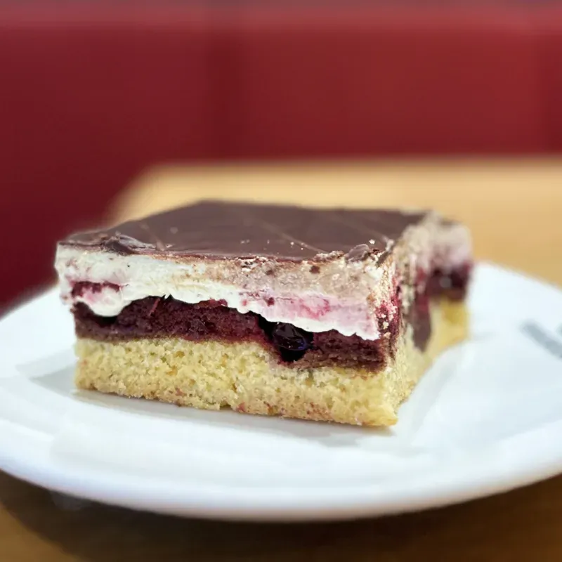 Stück Donauwelle mit Kirschen, Buttercreme und Schokoladenguss auf einem weißen Teller