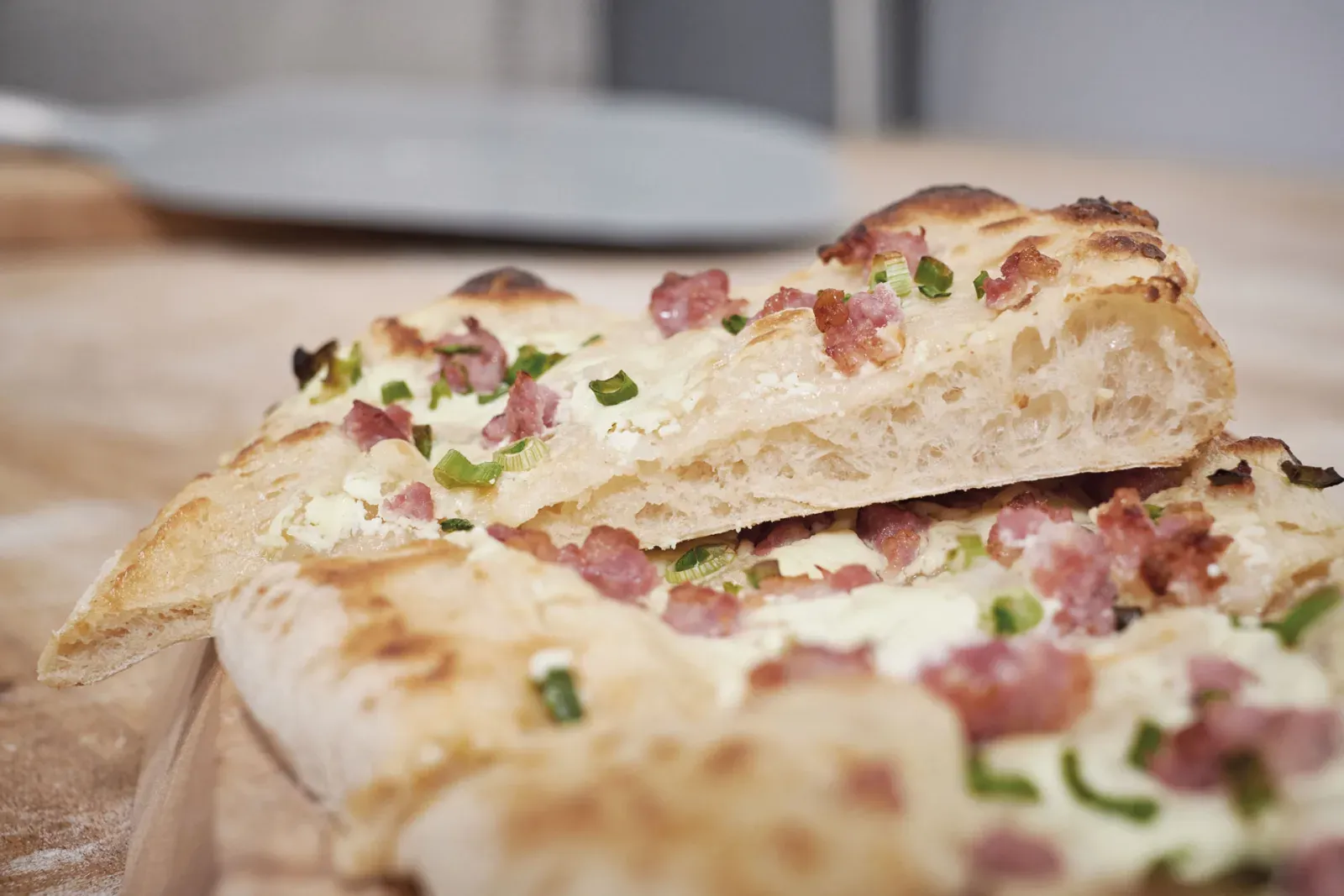 Schwäbischer Flammkuchen mit Schmand, Speckwürfeln und Frühlingszwiebeln, in Stücke geschnitten auf einem Holzbrett