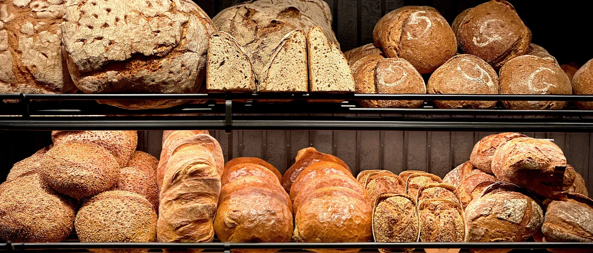 Zwei Regalböden voller Brote im Bäckerei-Café, von der runden Kruste bis zum aufgeschnittenen Laib