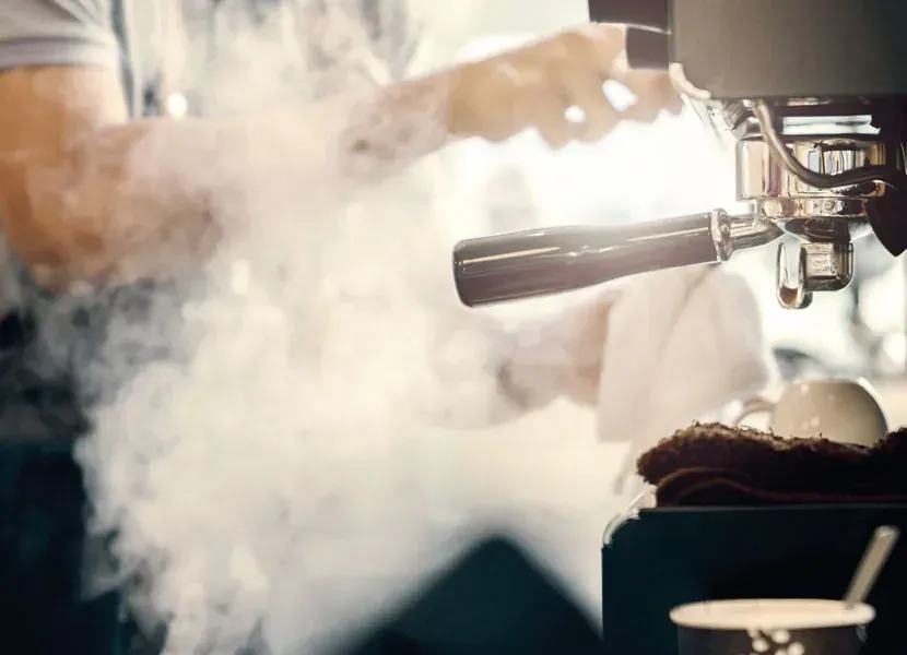 Dampf steigt aus der Milchdüse der Espressomaschine